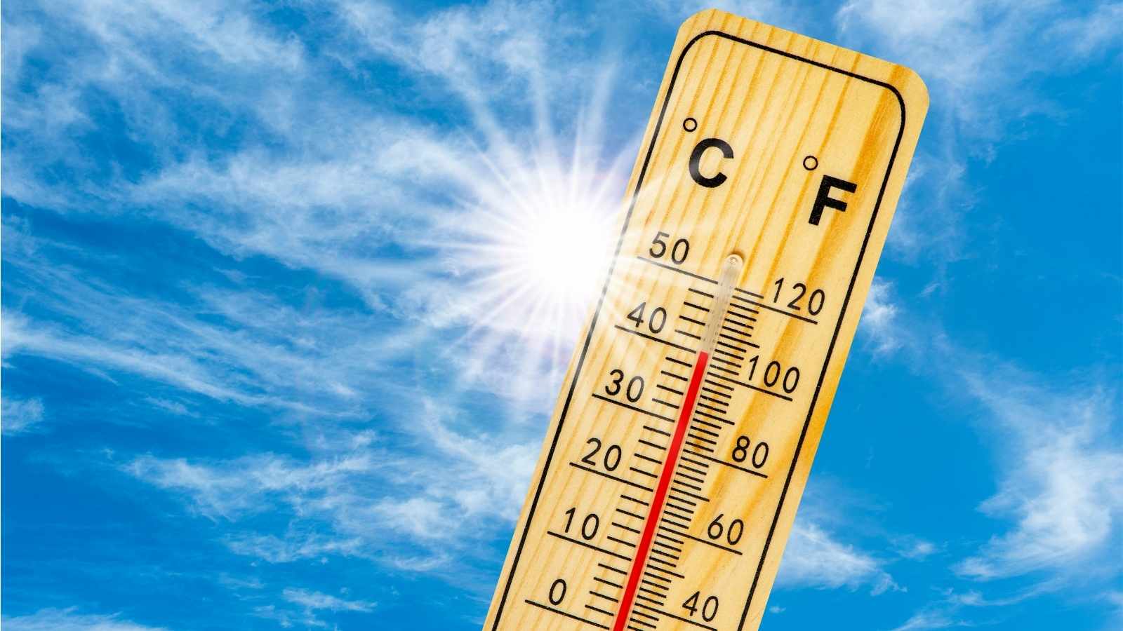 Close up of a thermometer showing a high heat with blue skies and bright sun in the background.
