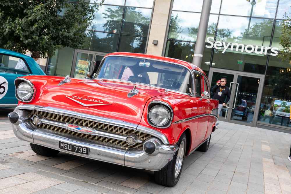 Red classic Chevrolet car parked outside a building with the sign "Seymours", displayed as part of a car show.