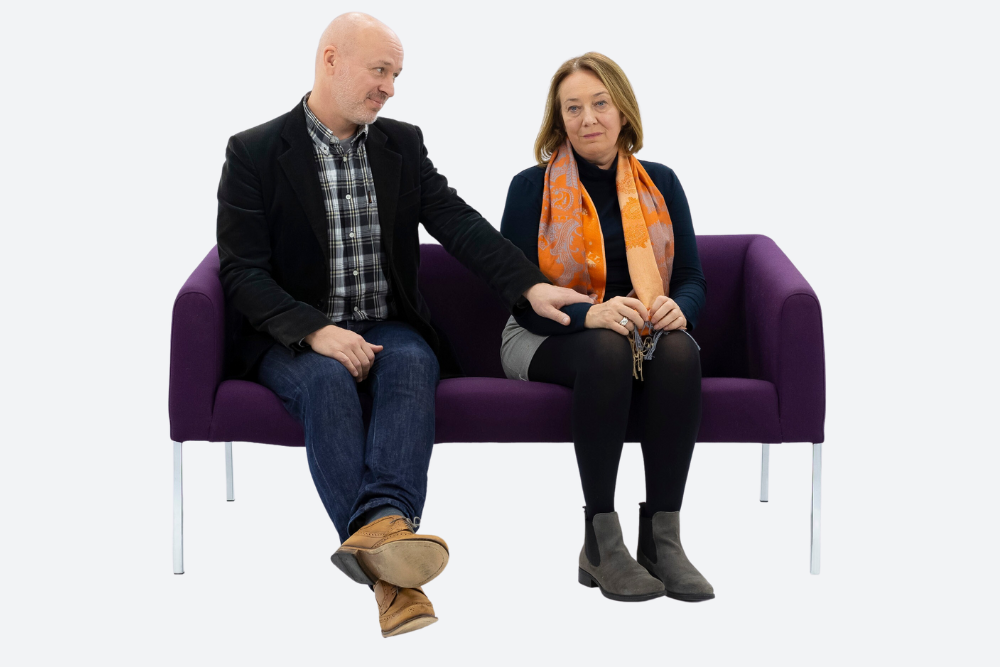A man and women sitting on a couch. The woman looks unhappy.