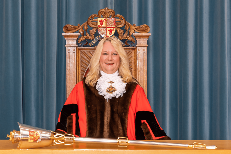 51st Mayor of Woking, Cllr Amanda Boote, wearing the ceremonial cloak and chain and sitting in the Mayoral chair with the a metal mace on a desk