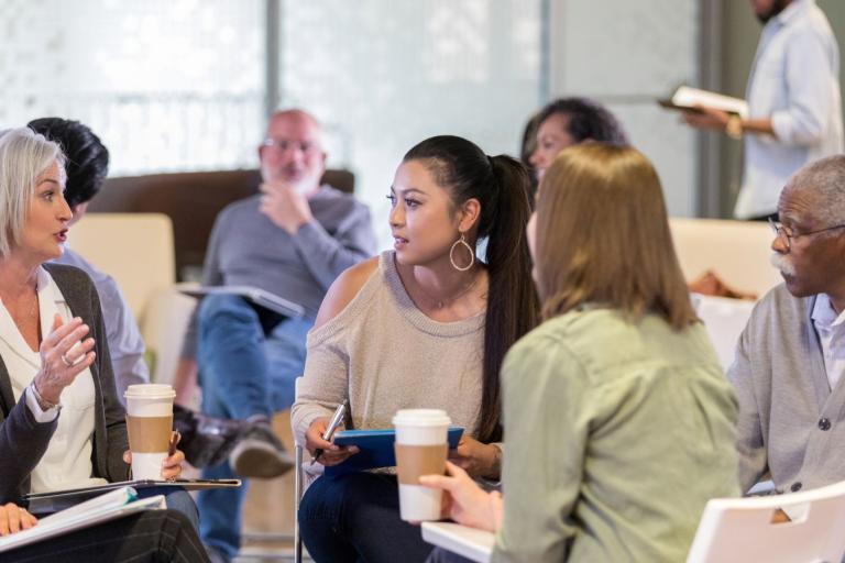 Four adults sitting on chairs in a circle having a discussion.