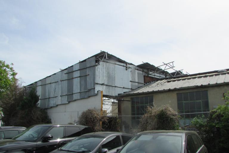 large front canopied enclosure made of scaffolding poles, corrugated metal sheeting, composite panels and a metal gate