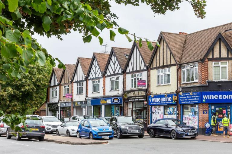 Parade of shops in Byfleet village with car parks in front.