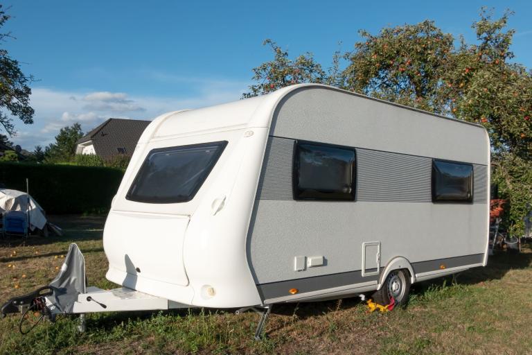 Single white caravan with windows parked in a green space.