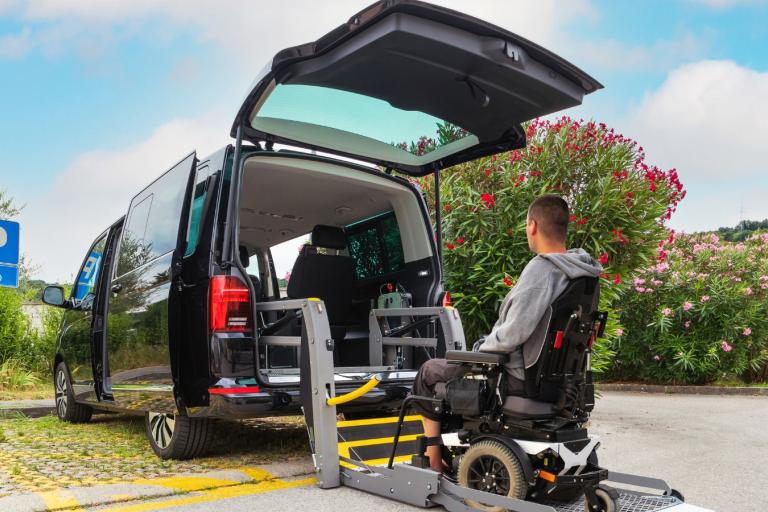 Man in wheelchair behind an accessible taxi with its boot open.