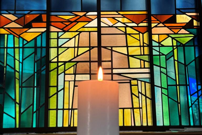 candle lit in front of stained glass window