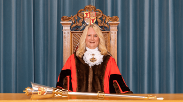 51st Mayor of Woking, Cllr Amanda Boote, wearing the ceremonial cloak and chain and sitting in the Mayoral chair with the a metal mace on a desk
