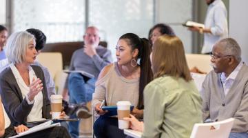 Four adults sitting on chairs in a circle having a discussion.