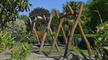 Outdoor play area swings surrounded by green plants.
