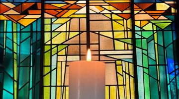 candle lit in front of stained glass window